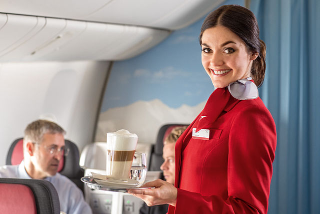 стюардесса австрийских авиалиний разносит кофе в салоне самолета, девушка улыбается