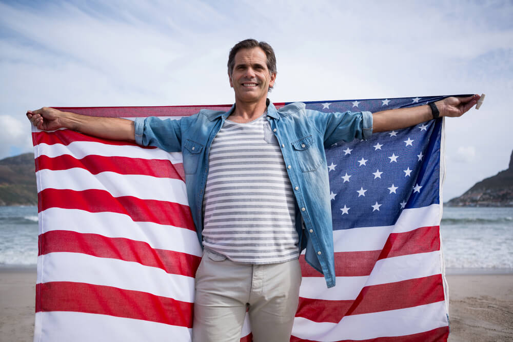 мужчина-америкацец в джинсовой рубашке с американским флагом в руках