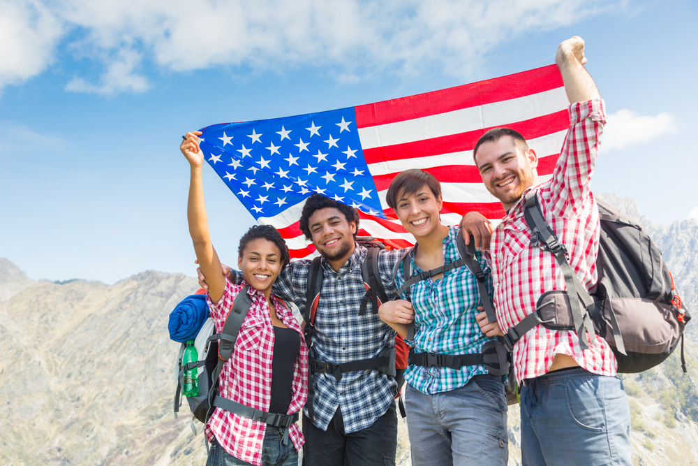 парни и девушки улыбаются с американским флагом над Гранд Каньоном в США - как живут ребята в Калифорнии