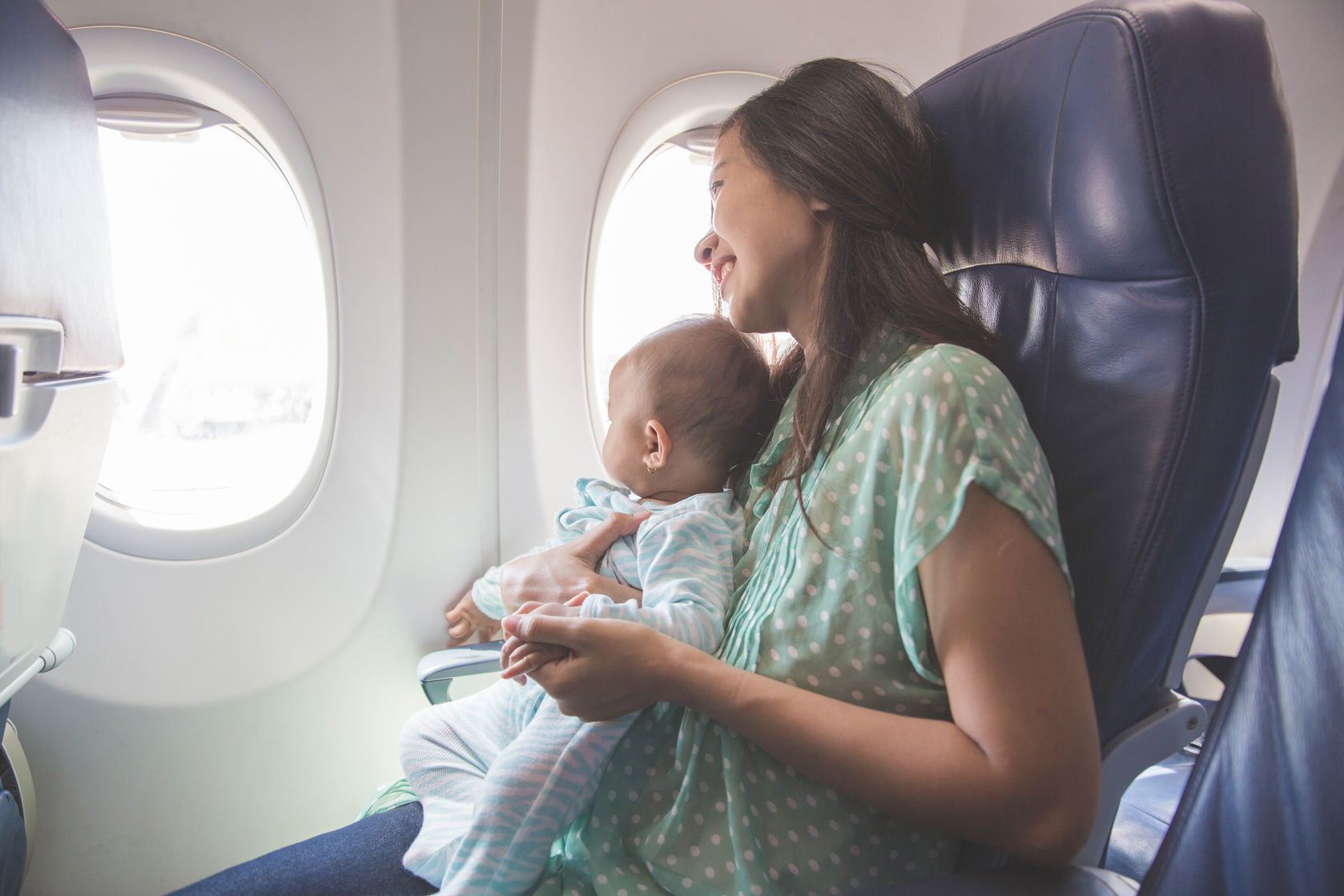 мама с грудным ребенком смотрит в иллюминатор самолета - родители с малышом во время полета