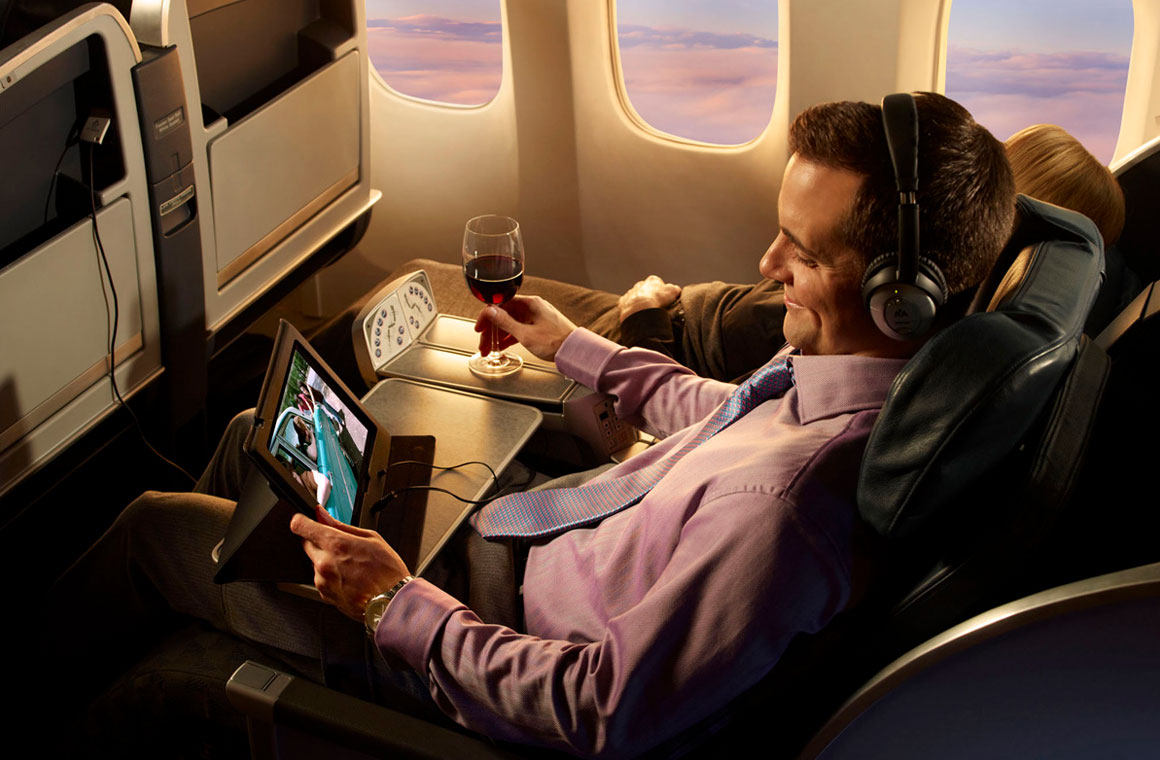мужчина смотрит фильм и пьет вино во время полета в первом классе самолета