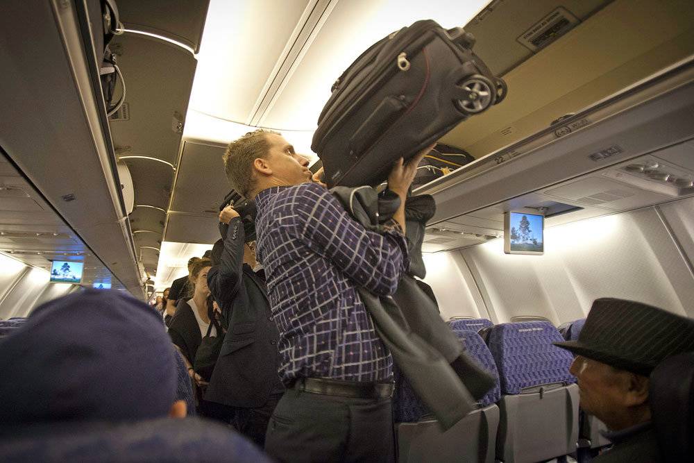 женщина кладе чемода на полку сверху в салоне самолета - девушка достает багаж с верхних полок в проходе на борту после посадки